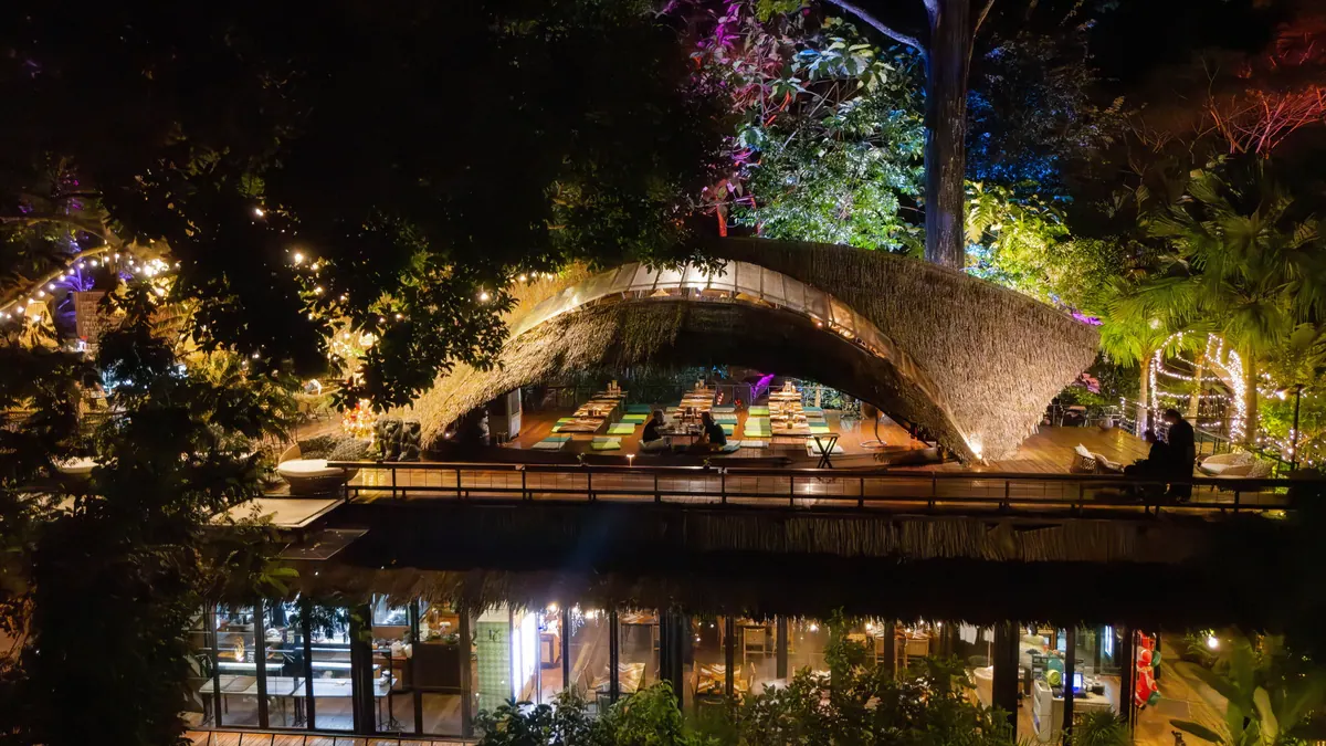 Curving illuminated restaurant roof and glass-fronted dining space at night