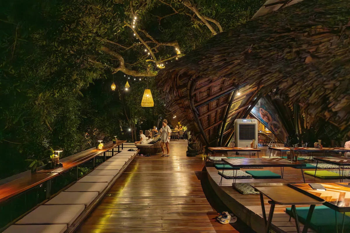 Wooden walkway between dining tables beneath trees and hanging lights